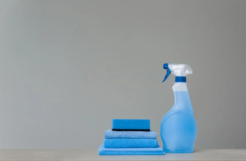 detergente, esponjas y trapos azules sobre una mesa gris