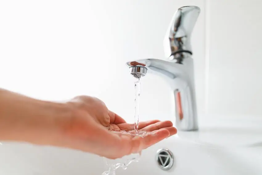 mano femenina mojándose con agua de un lavamanos